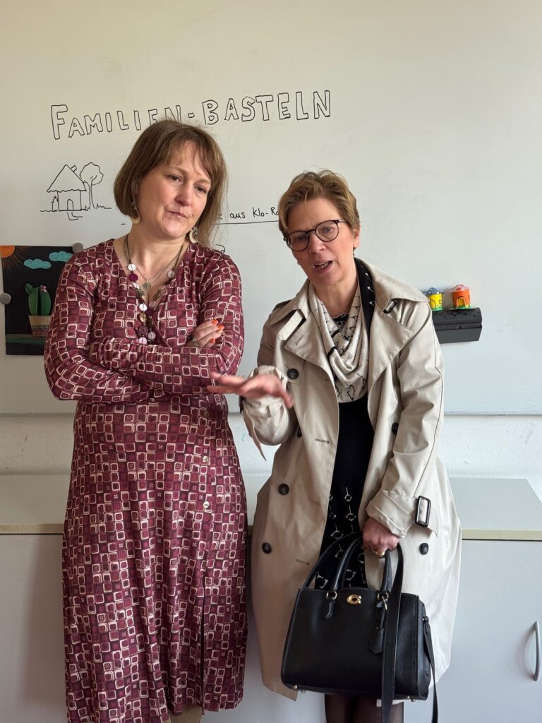 Senatorin Dr. Claudia Schilling mit einer Hand gestikulierend im Gespräch mit Lucie Horn vom QBZ Robinsbalje vor einer Tafel mit dem Schriftzug "Familienbasteln"