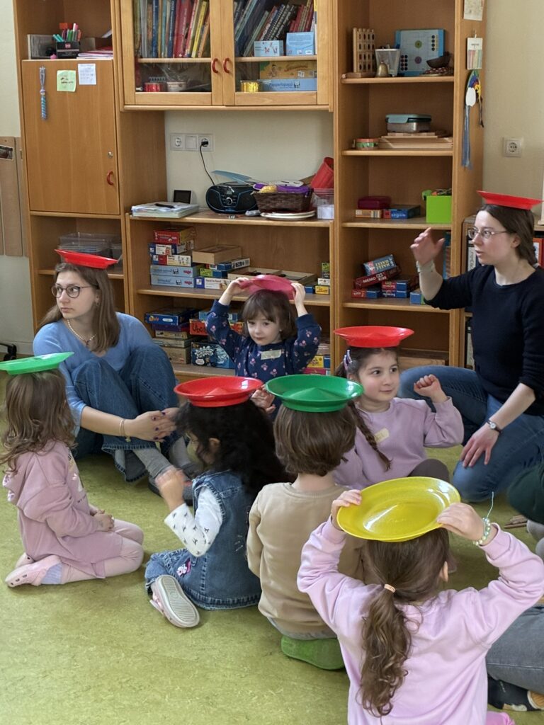 Die Kinder haben sich die bunten Jonglierteller auf den Kopf gesetzt und versuchen Balance zu halten.