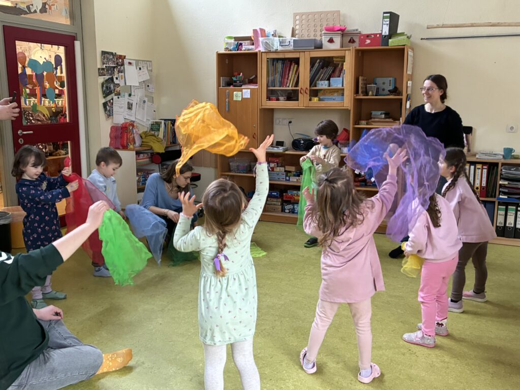 Die Kinder werfen im Kreis stehend ihre bunten Jongliertücher in die Höhe.