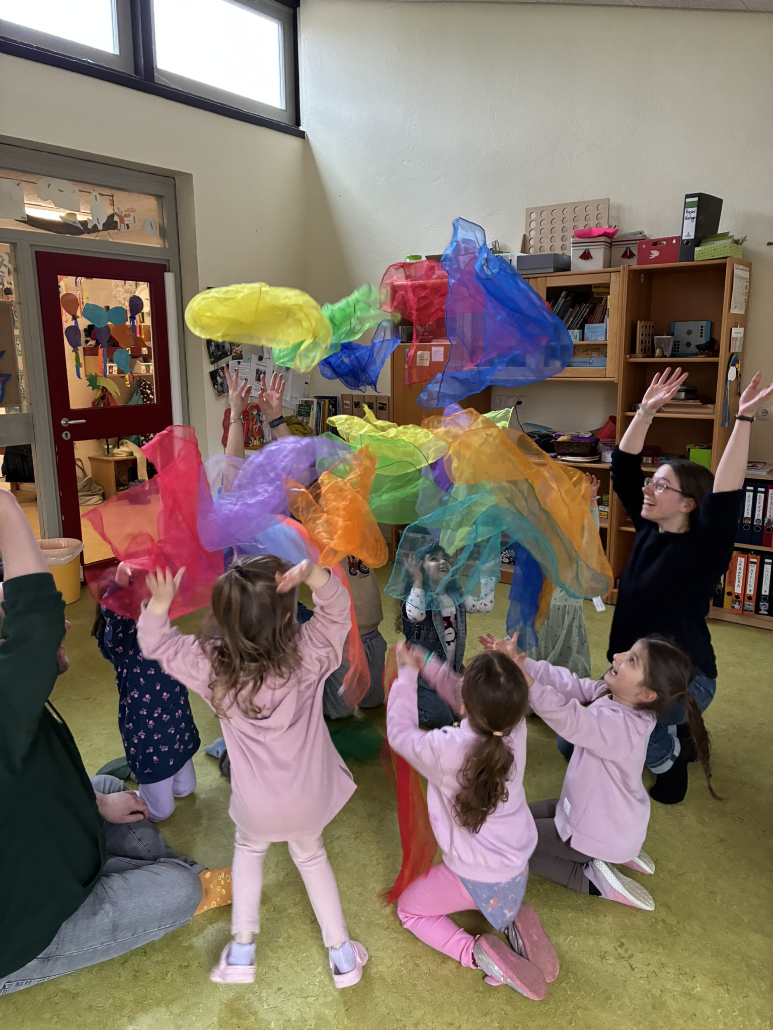 Die Kinder werfen im Kreis stehend alle gleichzeitig ihre bunten Jongliertücher in die Höhe - mit strahlenden Gesichtern.