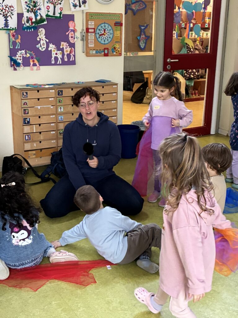 Die Reporterin von Radio Bremen ist auf dem Boden sitzend umringt von Kindern, mit denen sie ein Gespräch führt.