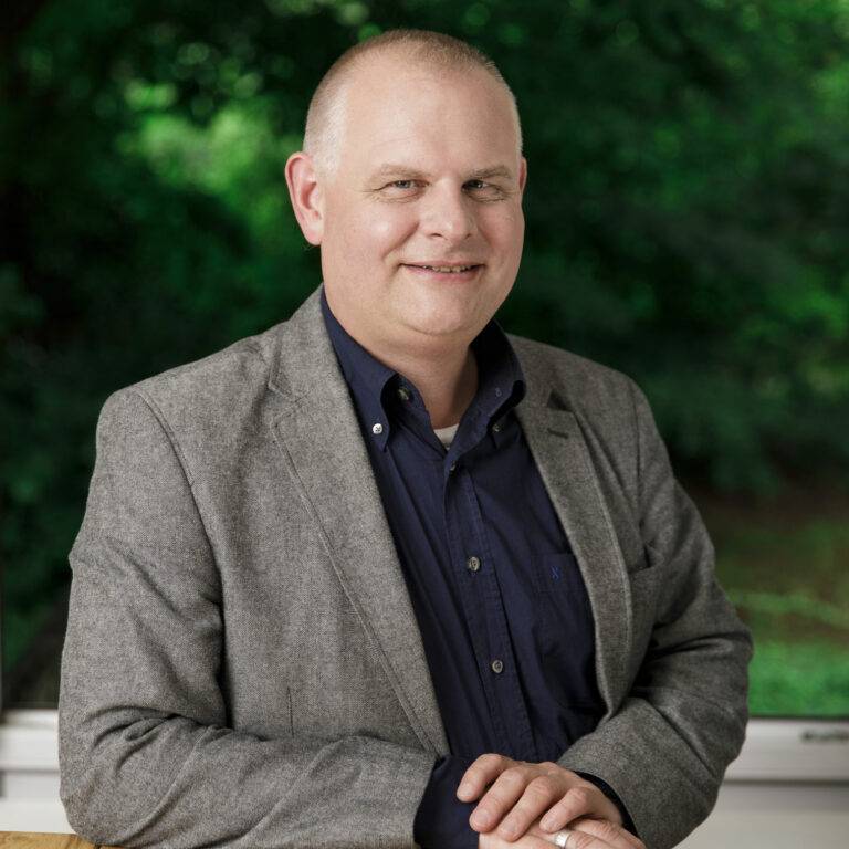 Matthias Emrich, Leiter Zentrale Dienste der Hans-Wendt-Stiftung, mit freundlichem Gesicht an einem Tisch lehnend