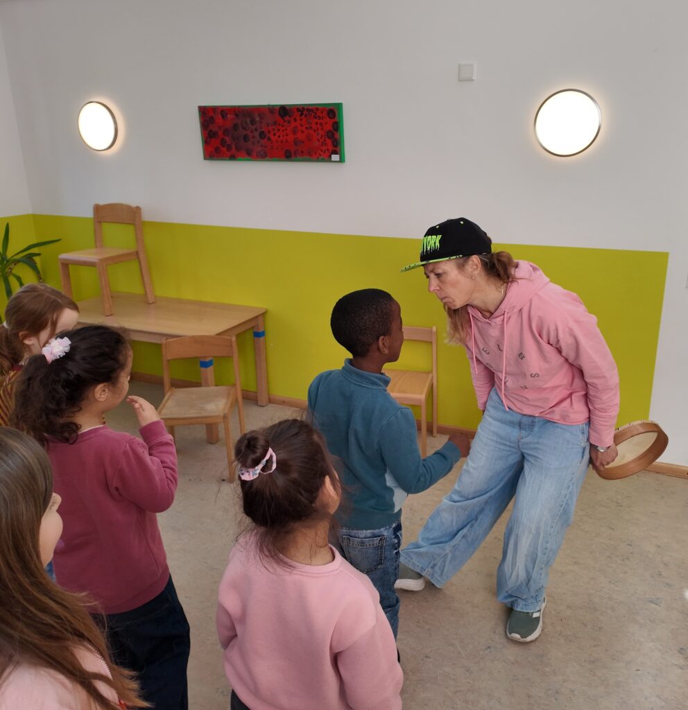 Eine Rollenspielsituation mit der Workshopleiterin in der Rolle der Provozierenden, die einen Jungen böse anschauend anspricht. Weitere Kinder schauen sich die Situation an mit dem Rücken zur Kamera.