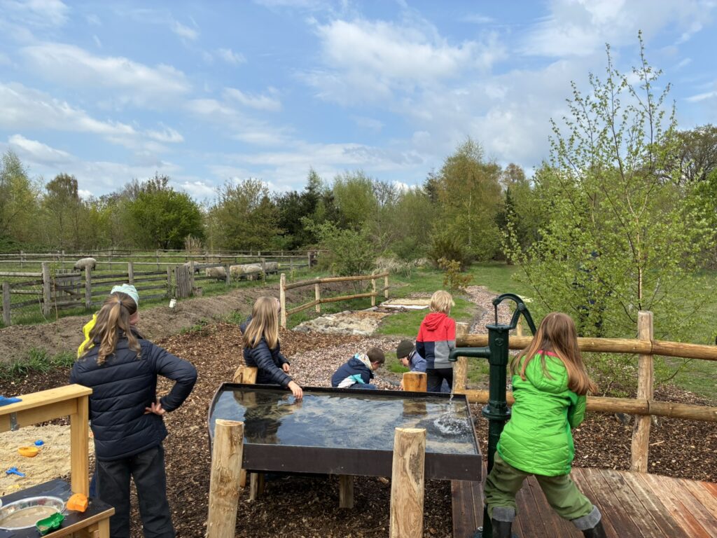 Kinder im Grundschulalter spielen an der Wasserpumpe.