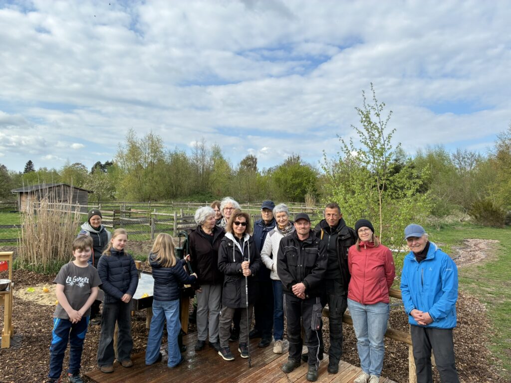 Gruppenbild mit Mitgliedern des KC Bremen Ginkgo stehen gemeinsam mit der Farmleitung, Kollegen aus dem Farmteam und Kindern einer Farmgruppe auf dem Wasserspielplatz vor der Pumpe.